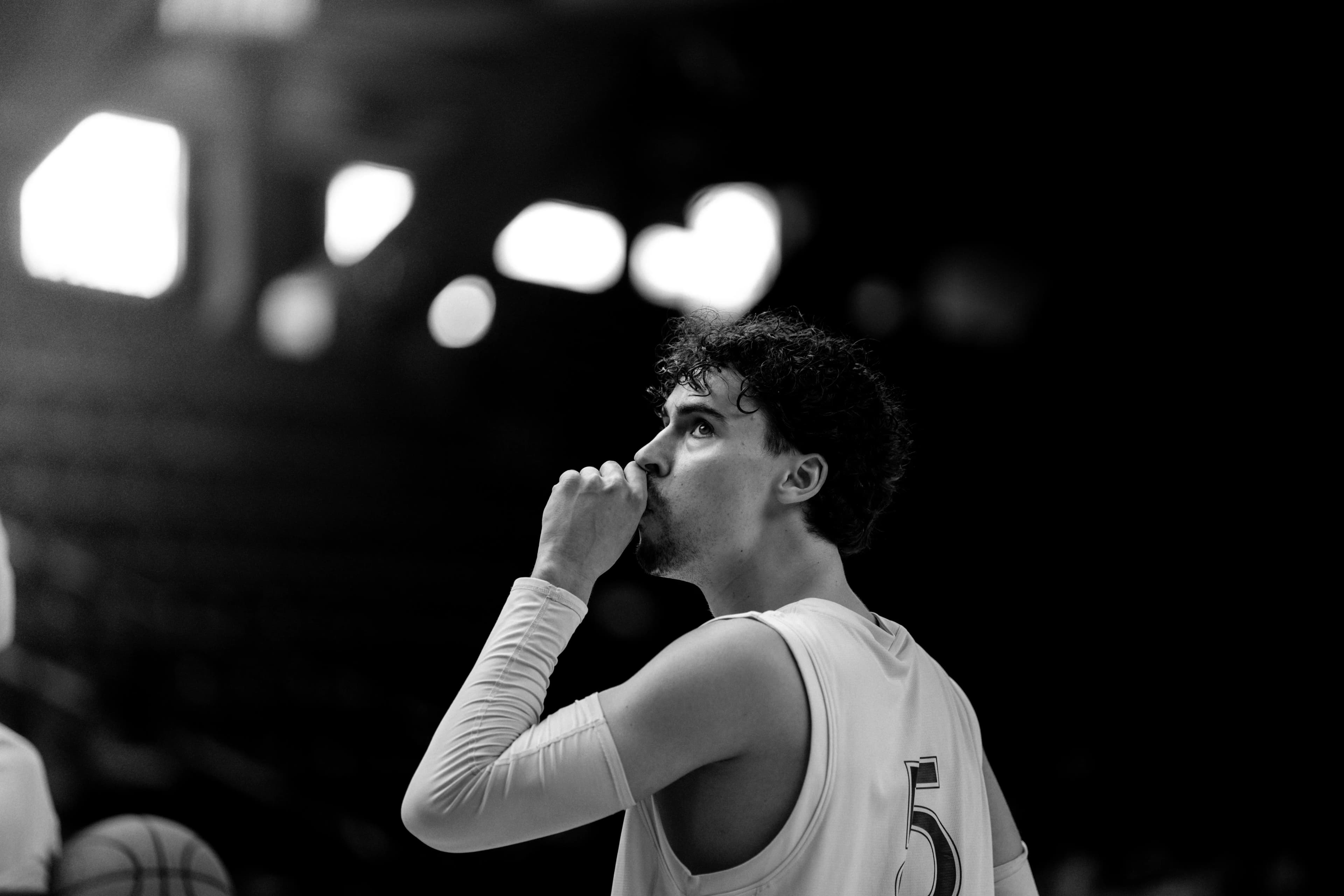 Schwarzweiß-Portrait: Basketballer Nummer 5 mit Compression Sleeve blickt nach oben in der Halle