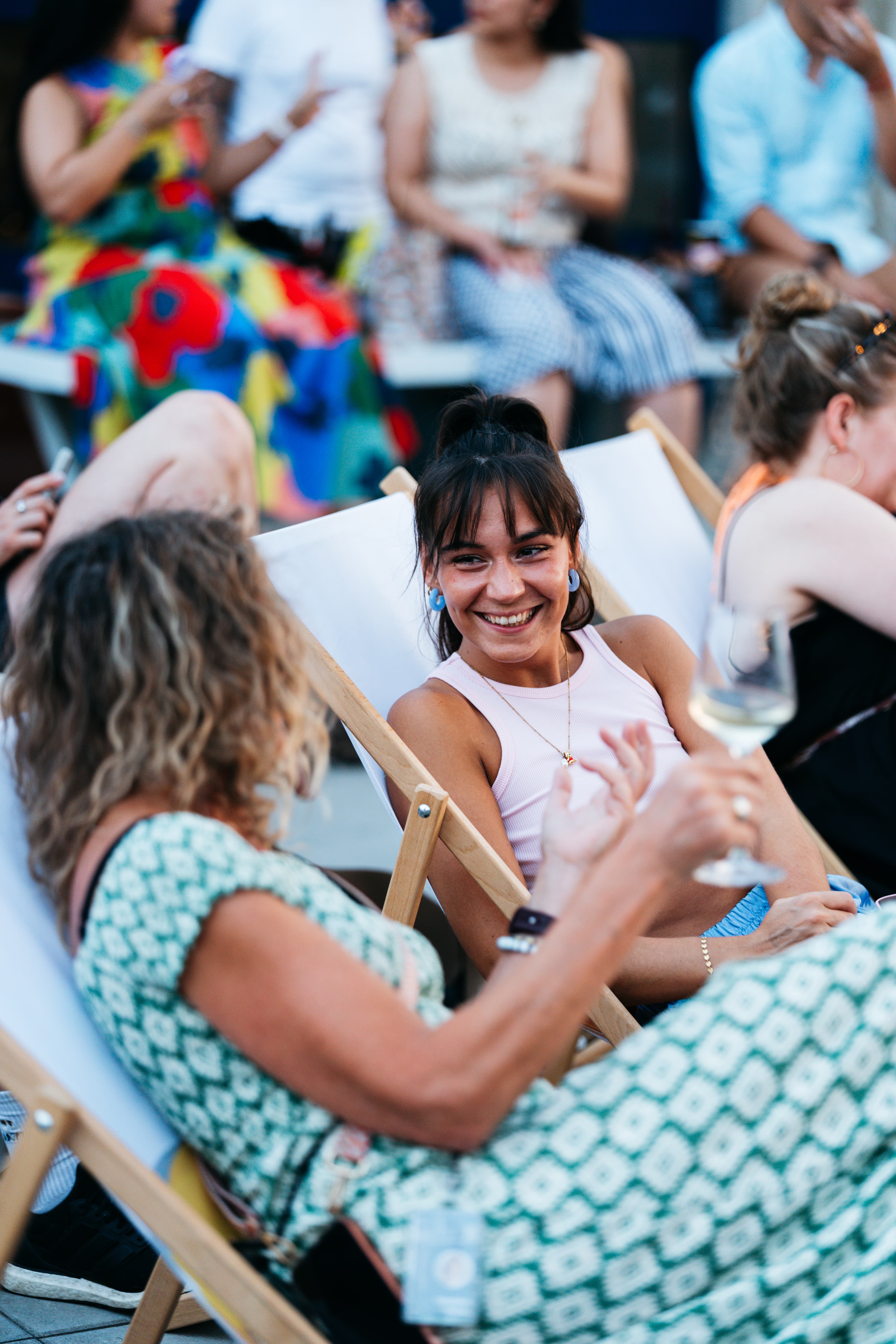 Zwei Frauen in Liegestühlen unterhalten sich lächelnd bei Wein auf dem rooftop office