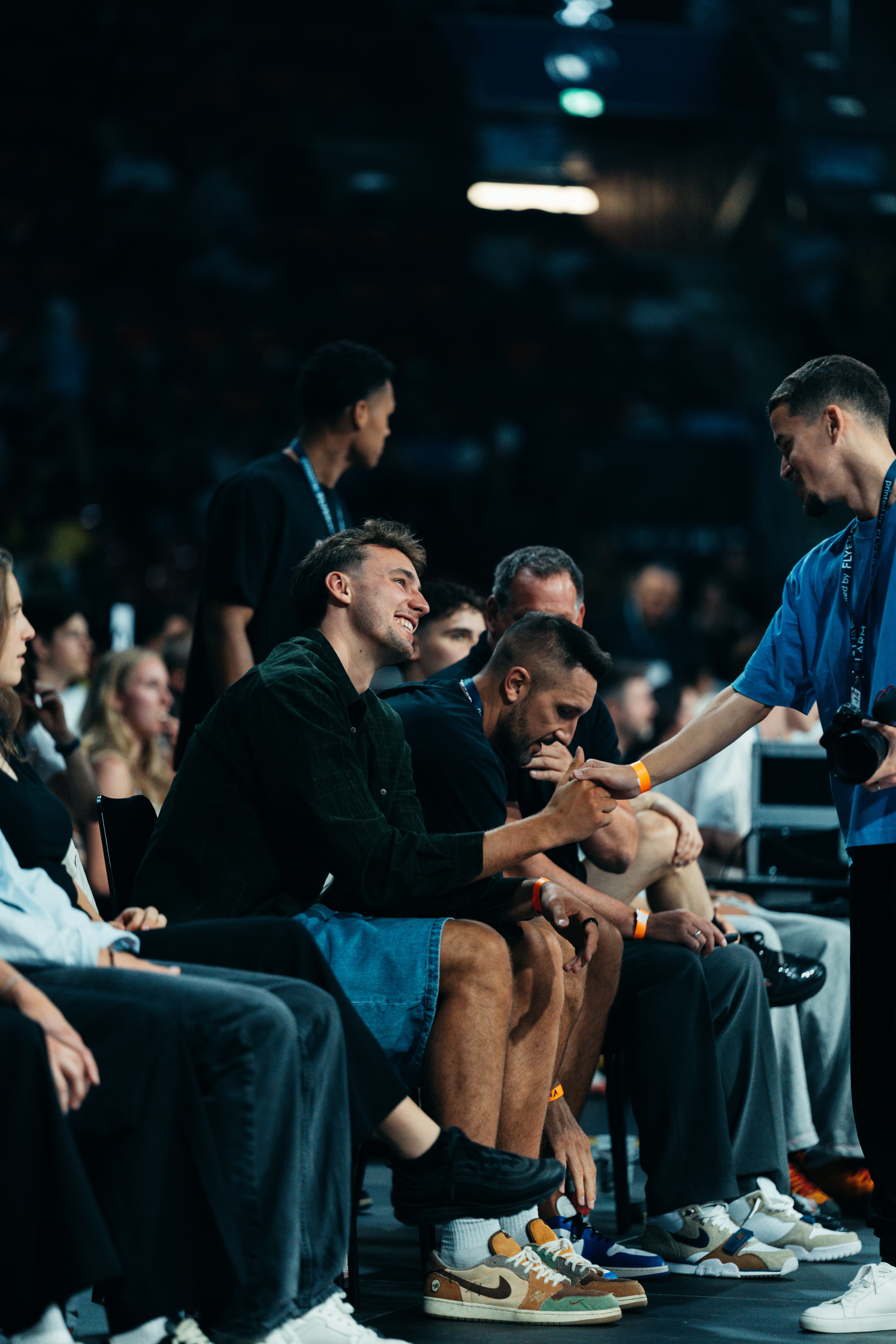 Fotograf im blauen Shirt schüttelt einem Gast in der ersten Reihe die Hand in der dunklen Arena