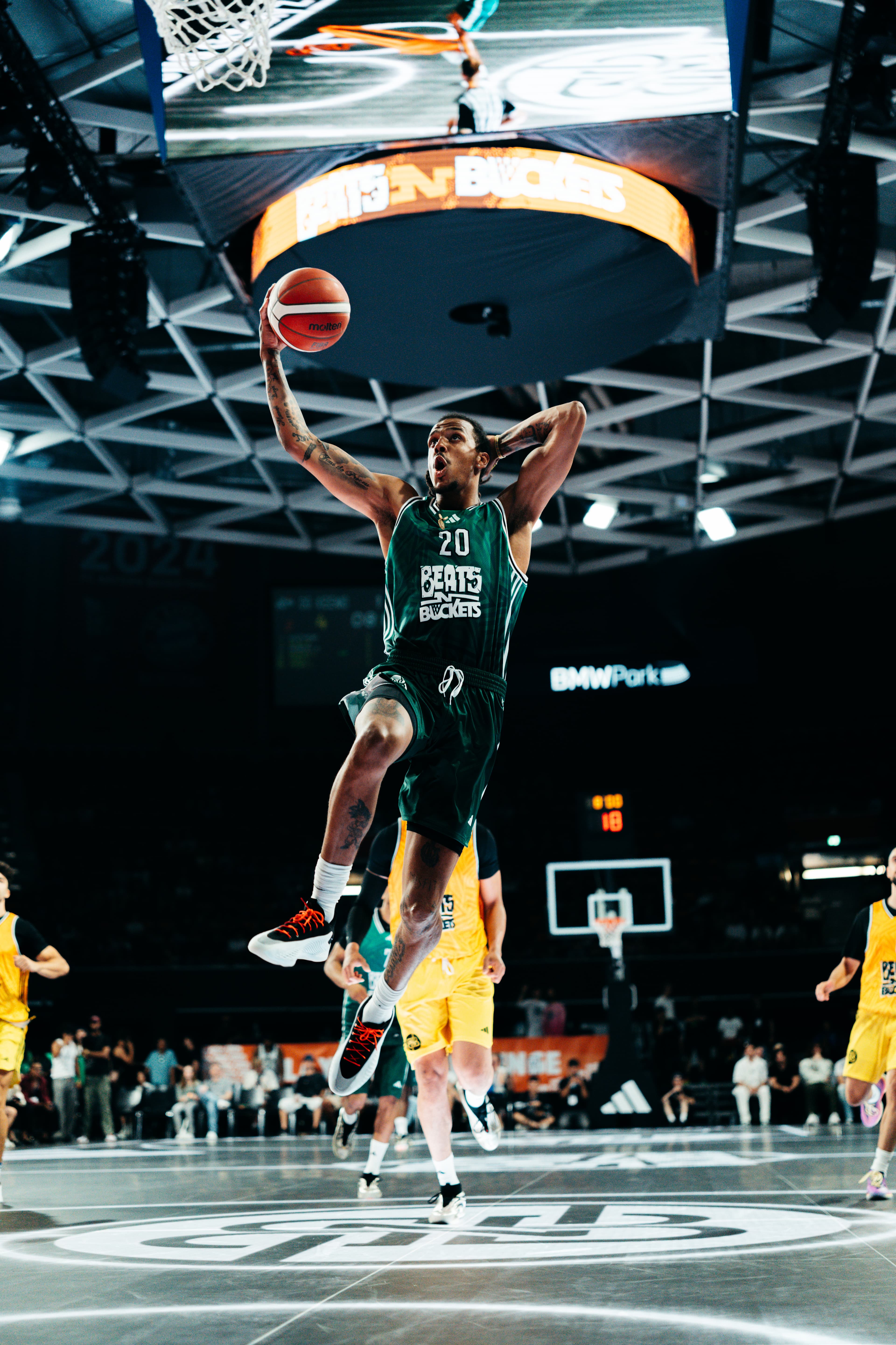 Spieler Nummer 20 in Grün im Dunk-Sprung über dem Court, BMW-Park-Schild und Jumbotron oben