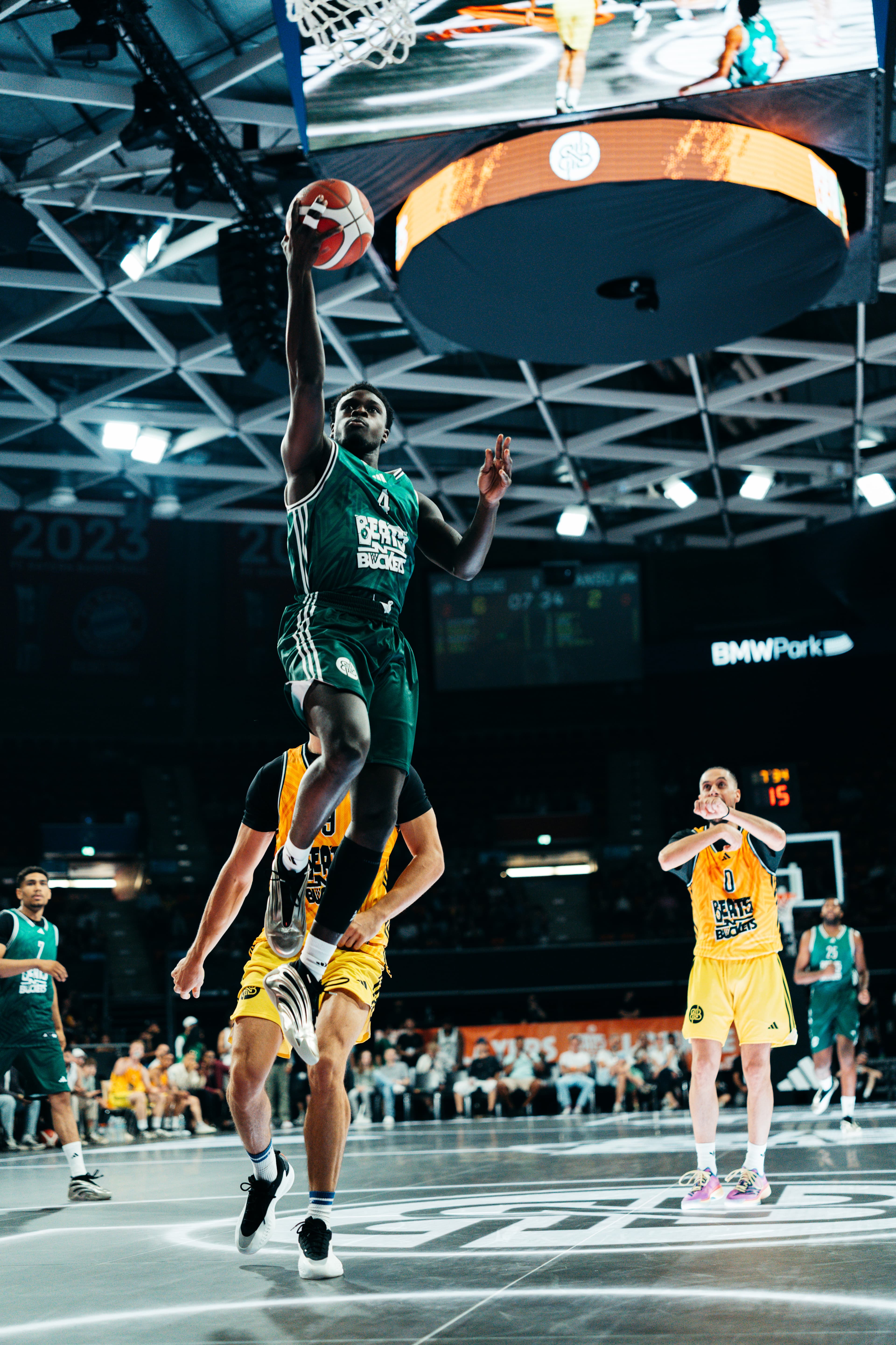 Spieler Nummer 4 der Veolia Towers Hamburg im Dunk-Sprung, gelbe Gegner und BMW Park hinter ihm