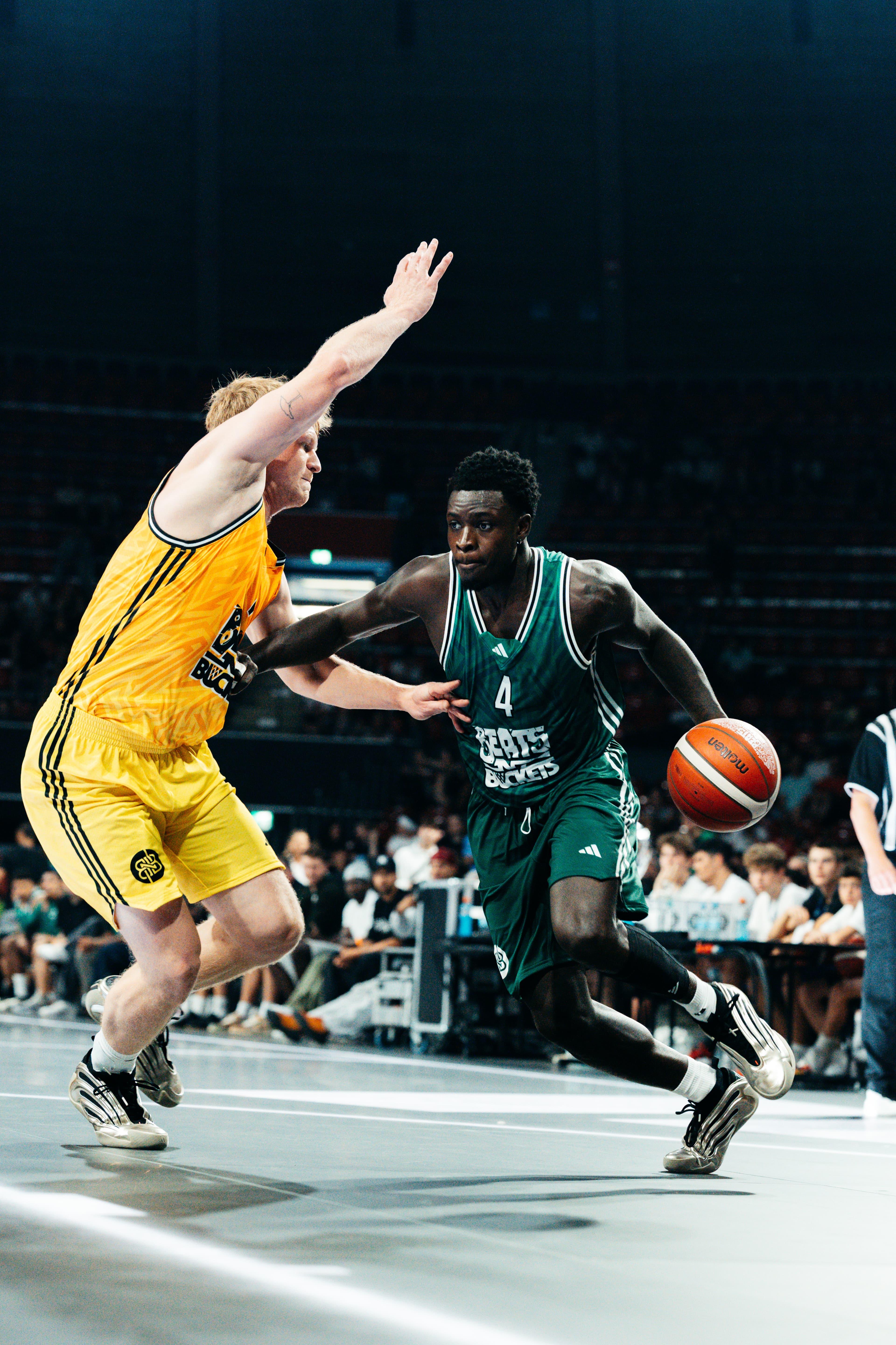 Drive: Spieler Nummer 4 in Grün dribbelt gegen Verteidiger in Gelb vor dunkler Crowd