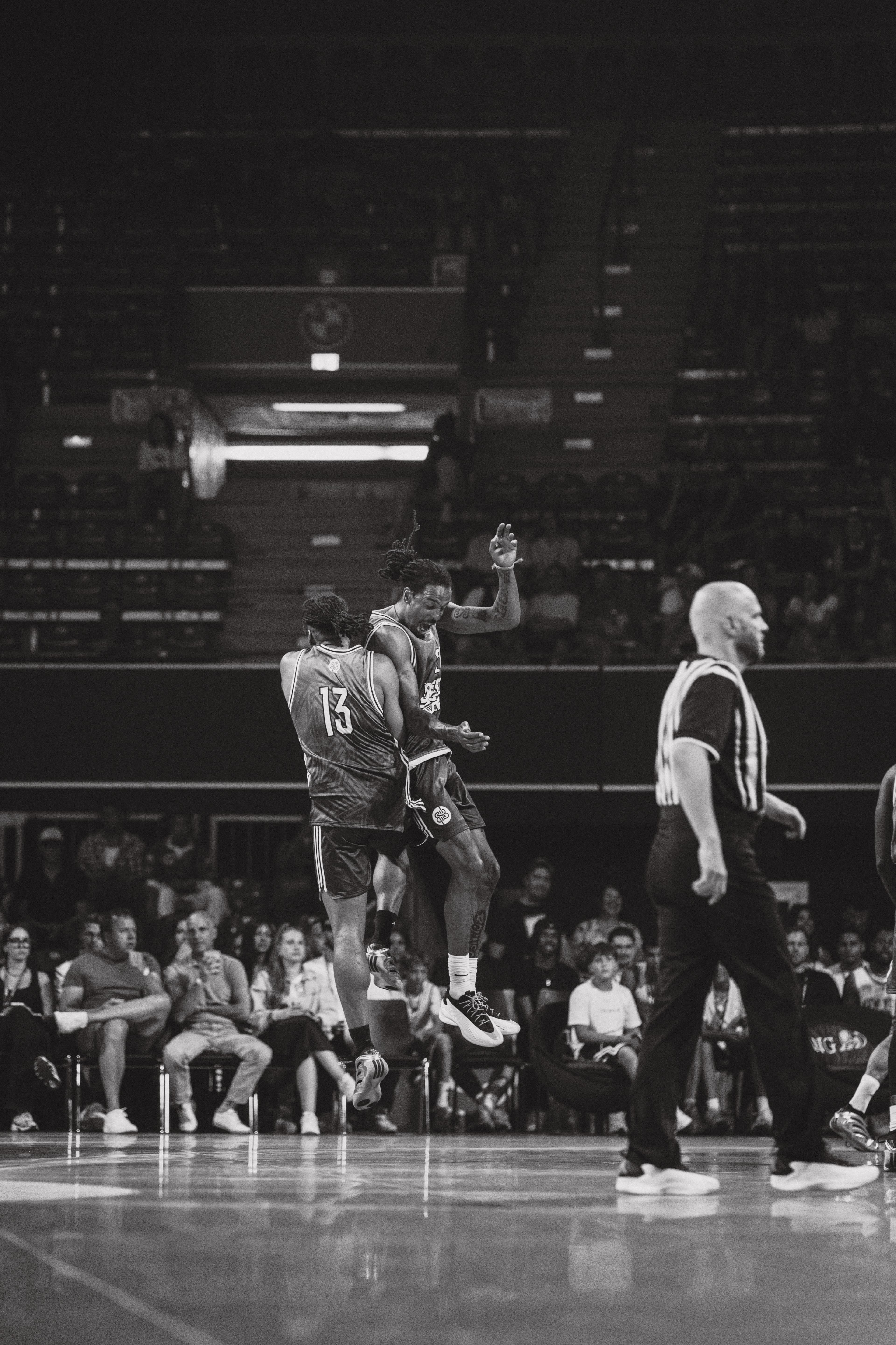 Black and white: two basketball players mid-jump at BMW Park, referee in the foreground