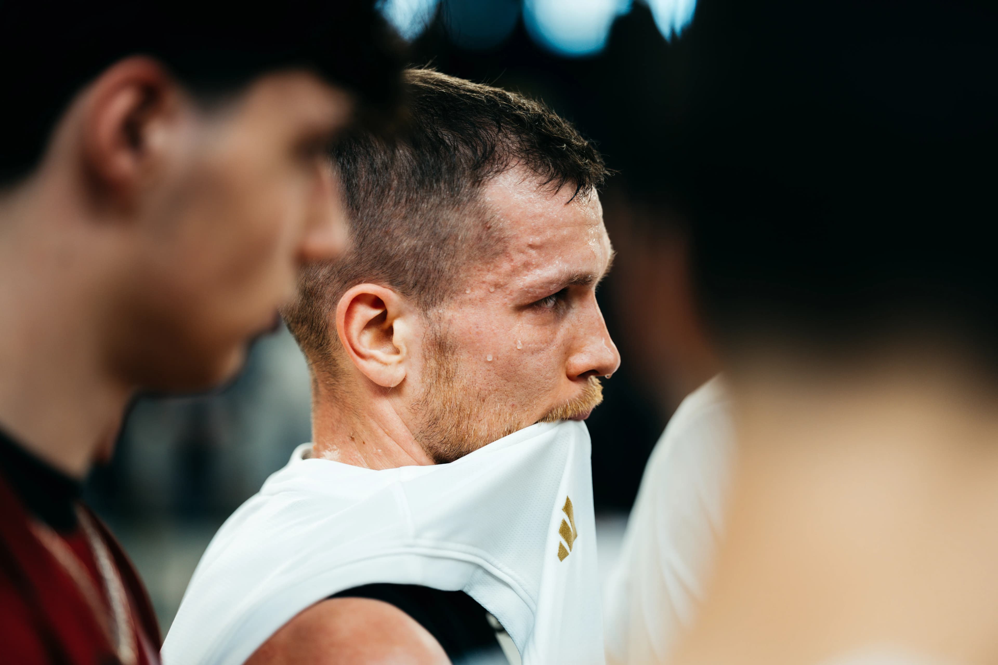 Close-up of a sweating player pulling his white jersey over his mouth, arena softly blurred behind