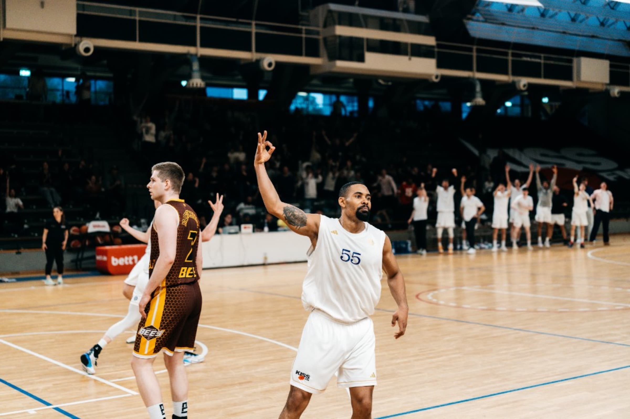 Player number 55 signalling OK after a three-pointer, crowd and bench in the background
