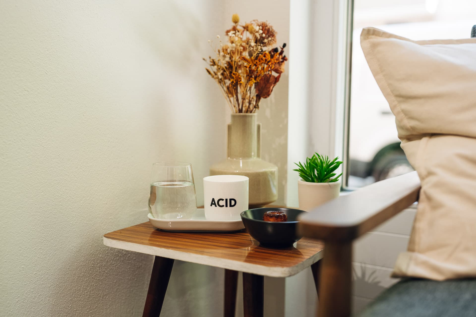 Beistelltisch mit Wasserglas, Kerze, Canelé und Trockenblumen am Fenster im Salon