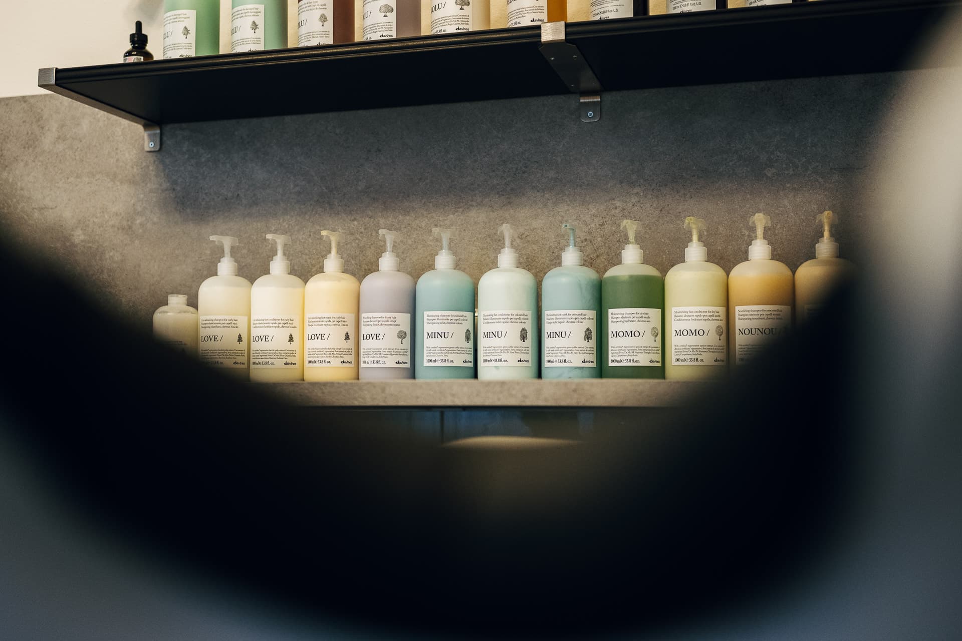 Row of pastel Davines haircare bottles on a grey shelf at Charles Edward salon