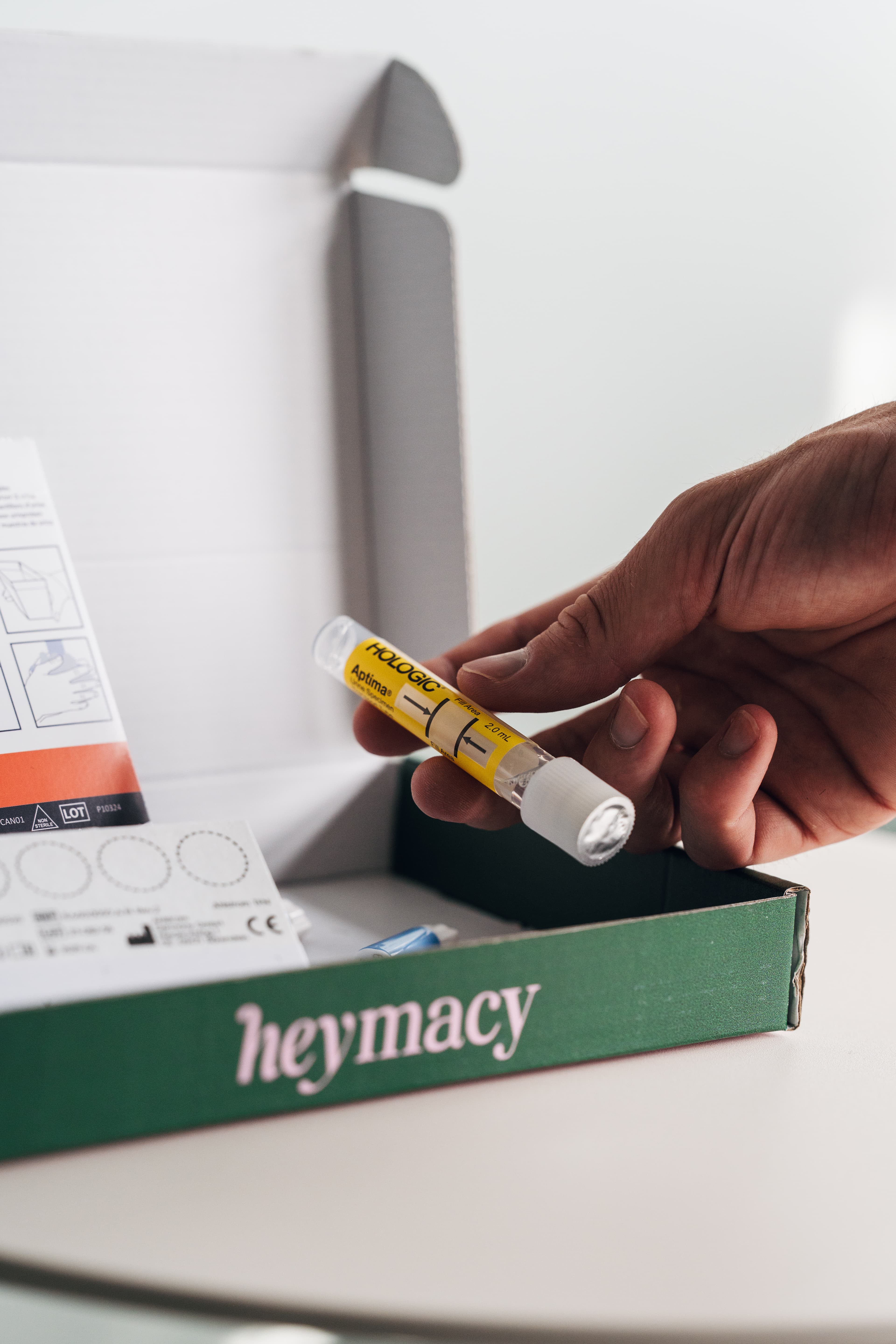 Hand hält klares Teströhrchen mit gelbem Etikett über der geöffneten heymacy-Box