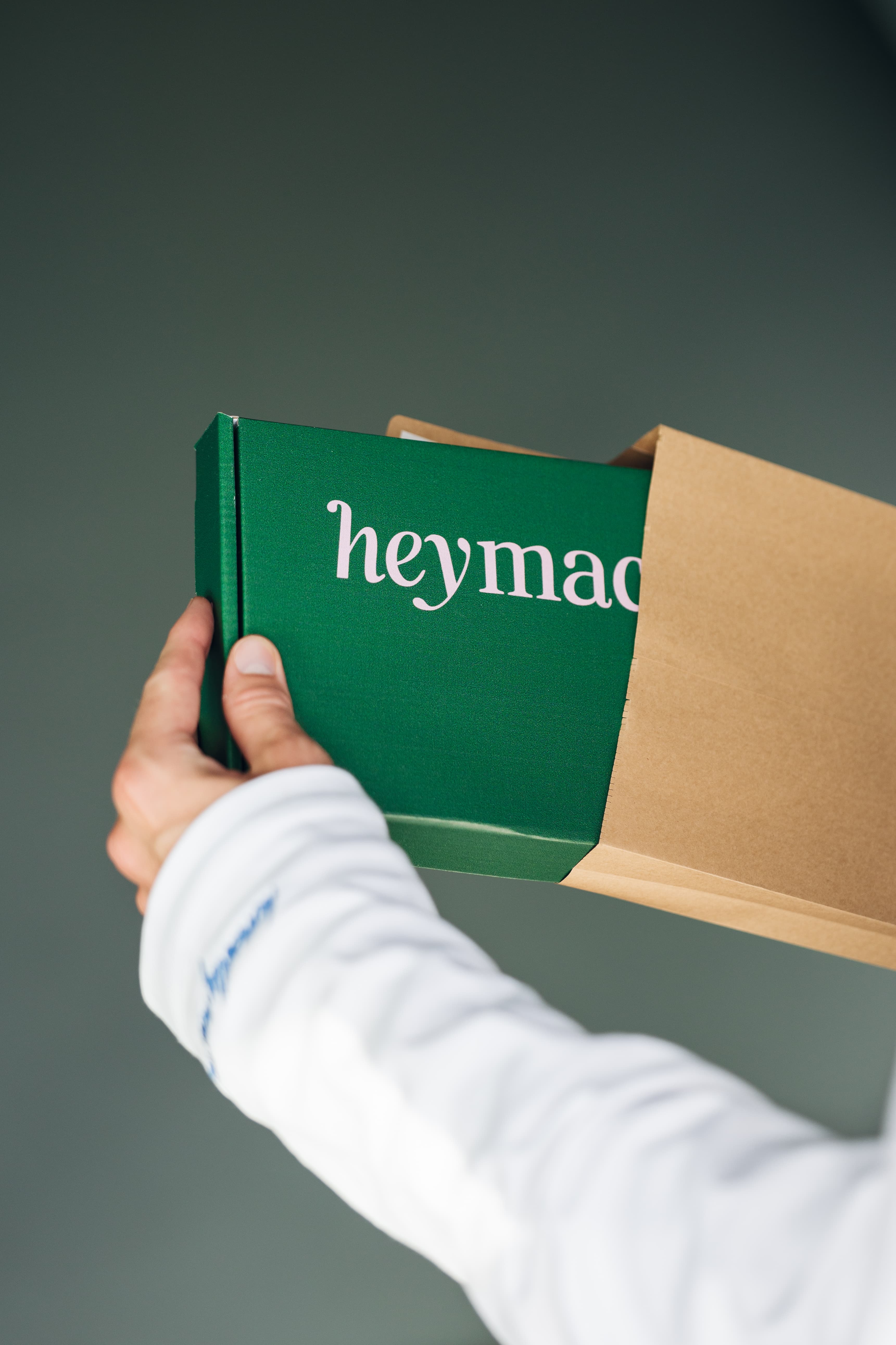 Hand zieht die dunkelgrüne heymacy-Box aus einem braunen Papier-Mailer