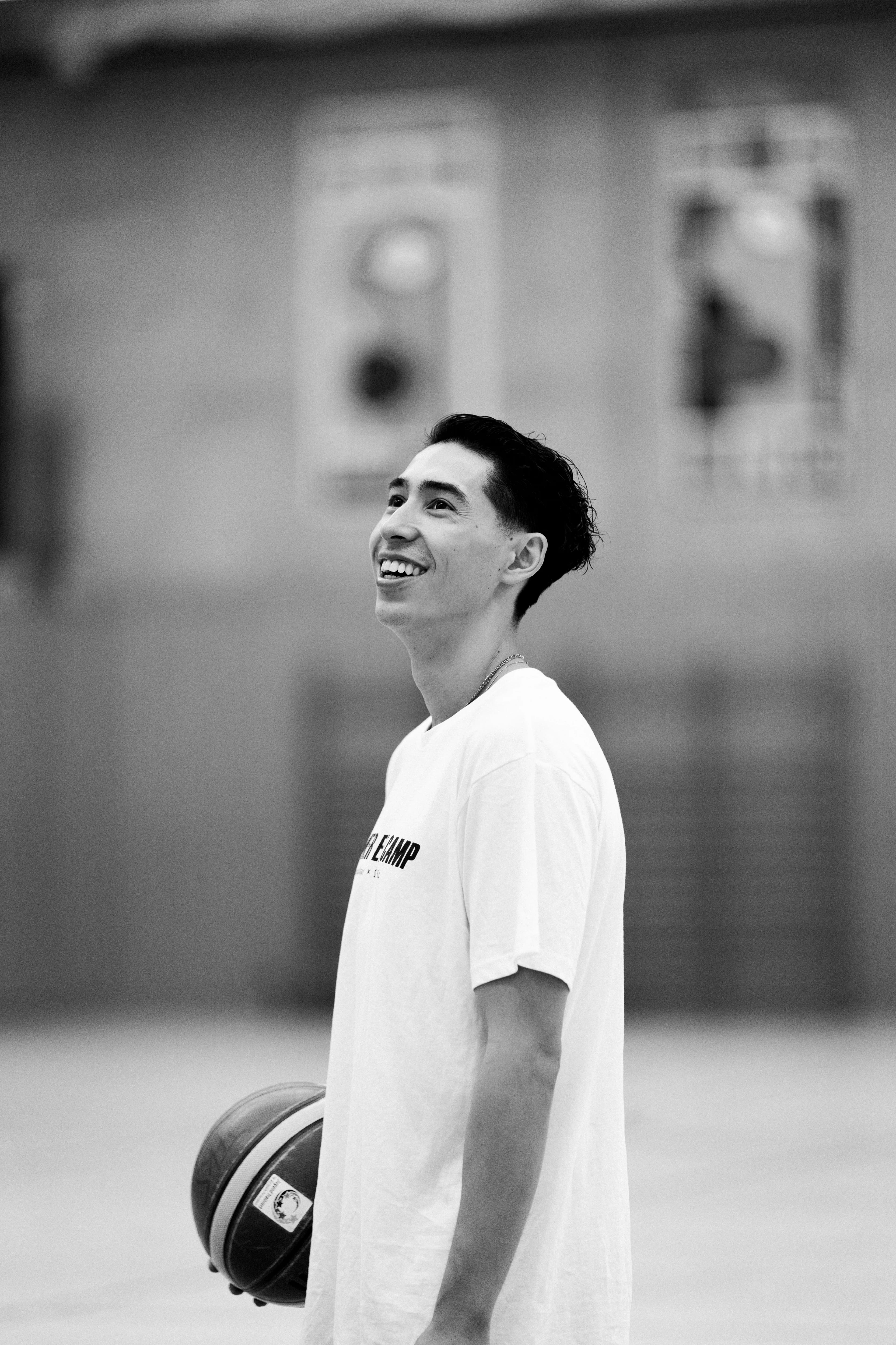 Black and white: smiling camp participant with a basketball under his arm in the gym
