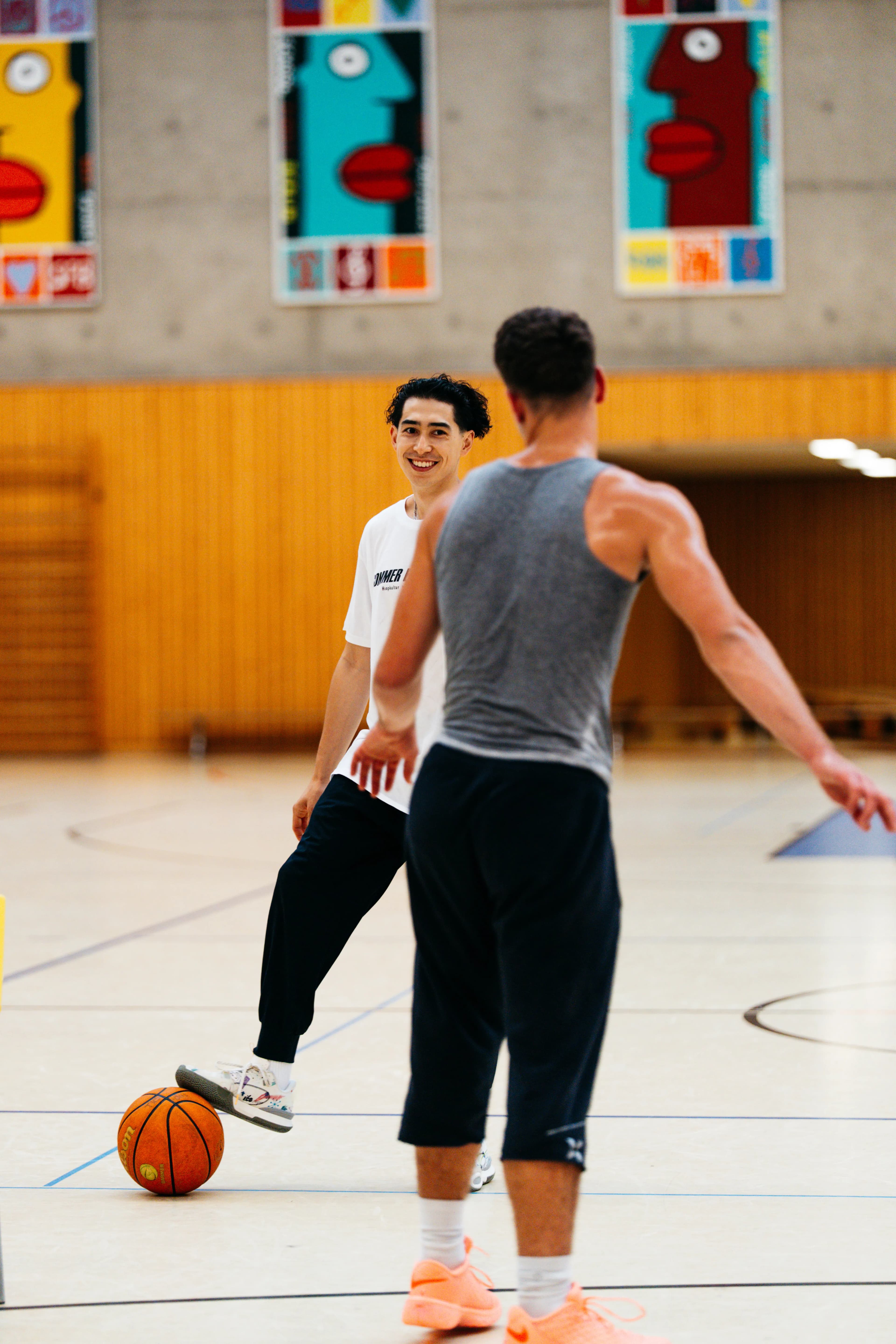 Two players talking on the court, orange ball and pop-art posters on the wall