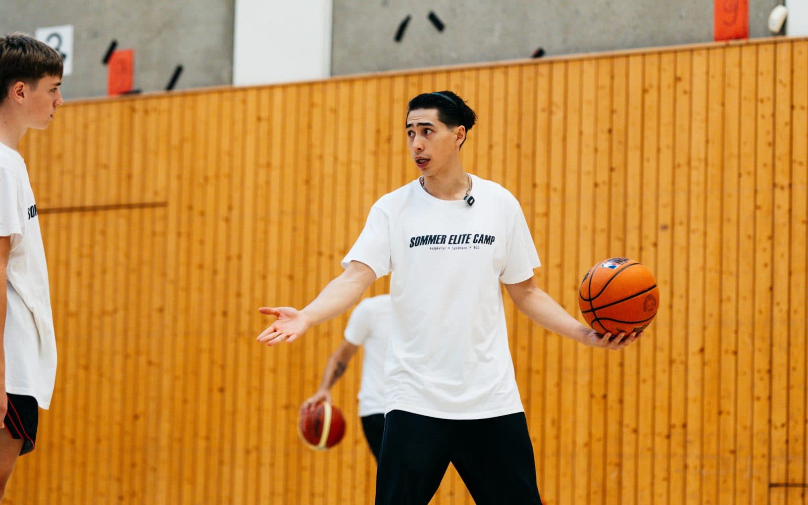 Coach mit Basketball gestikuliert beim Sommer Elite Camp von Hoopkultur in der Trainingshalle