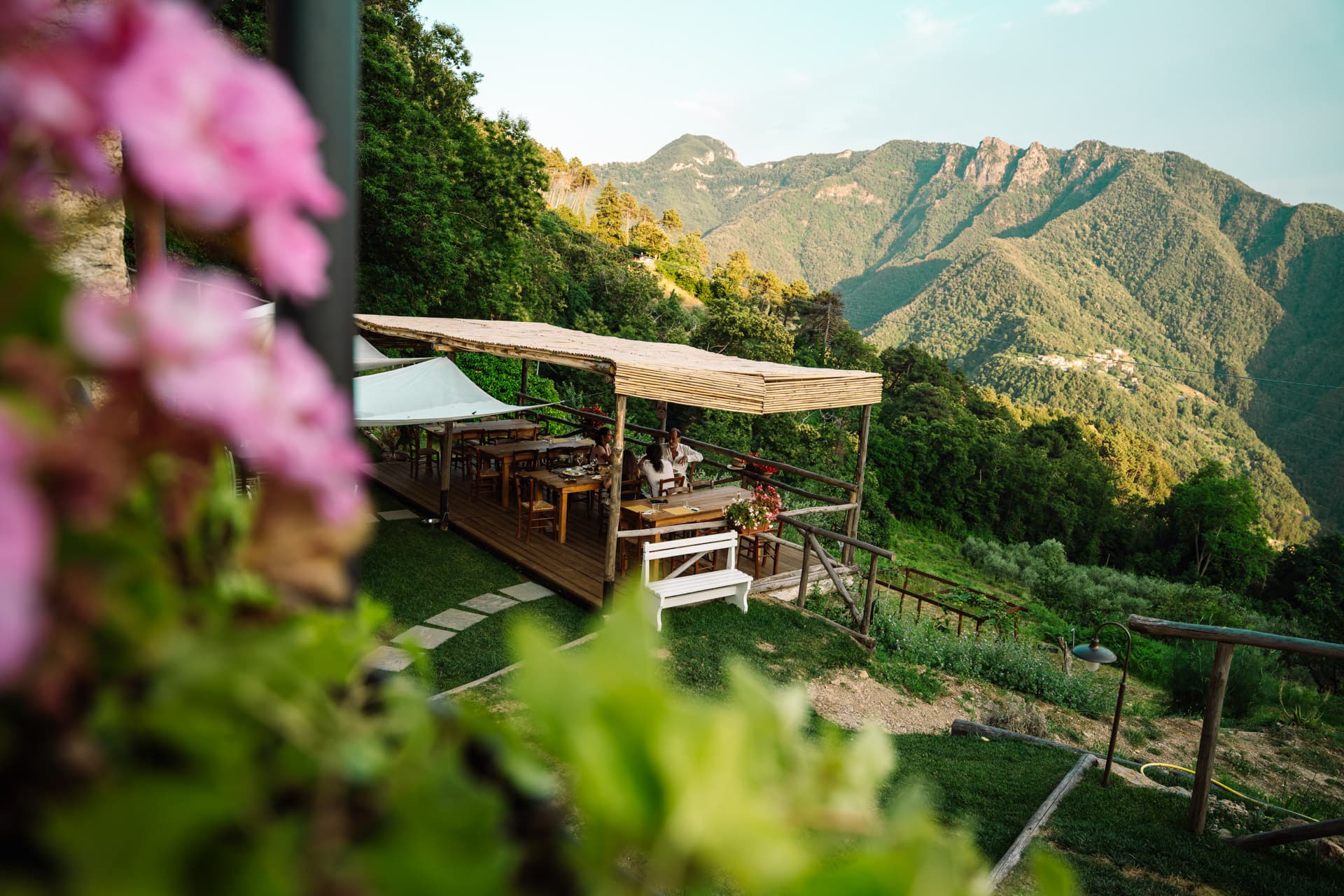 Wooden terrace at La Posa del Mulo overlooking forested Apuan Alps, guests at timber tables