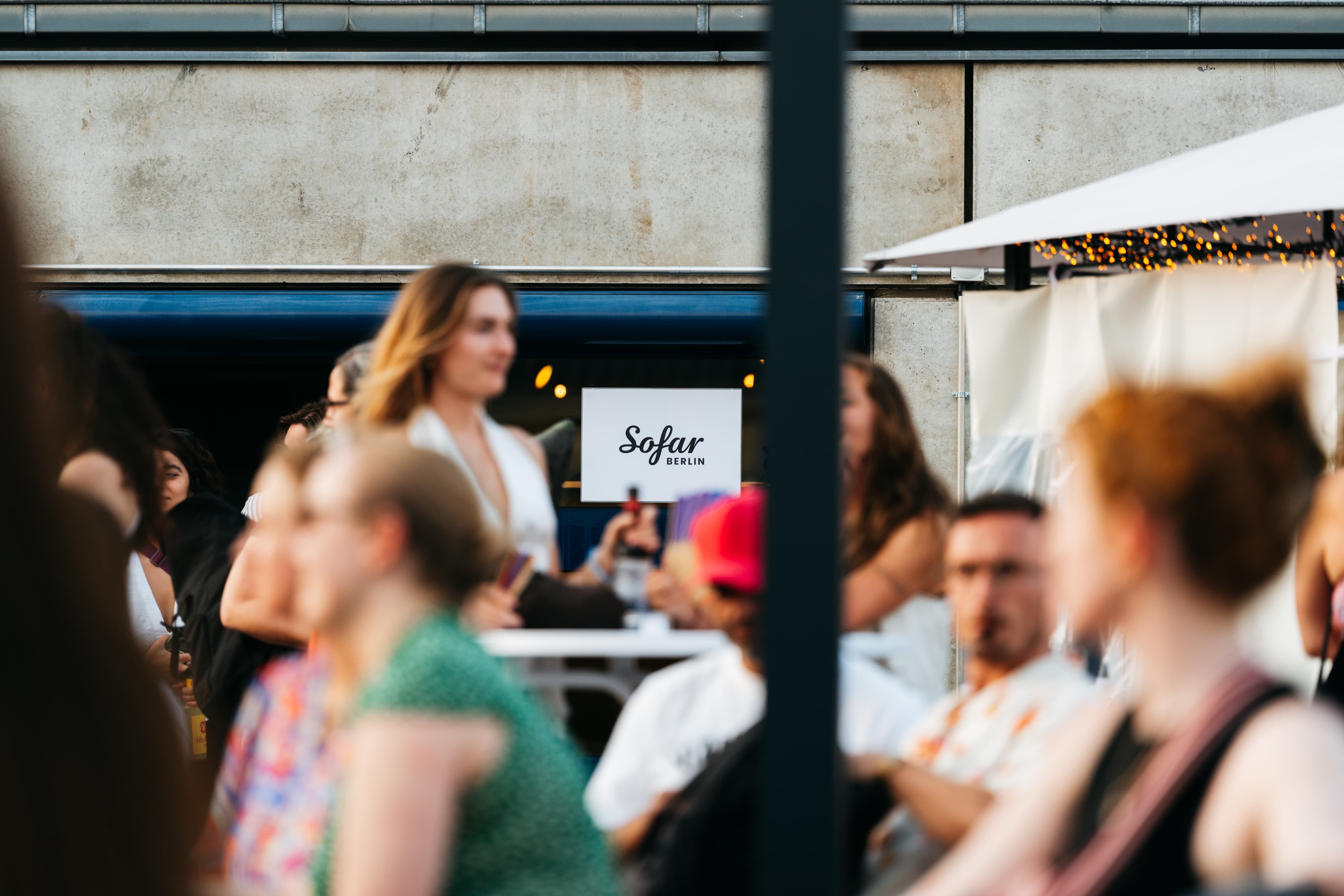 Guests at a Sofar evening in Moabit, Sofar Berlin sign in focus, fairy lights on a tent